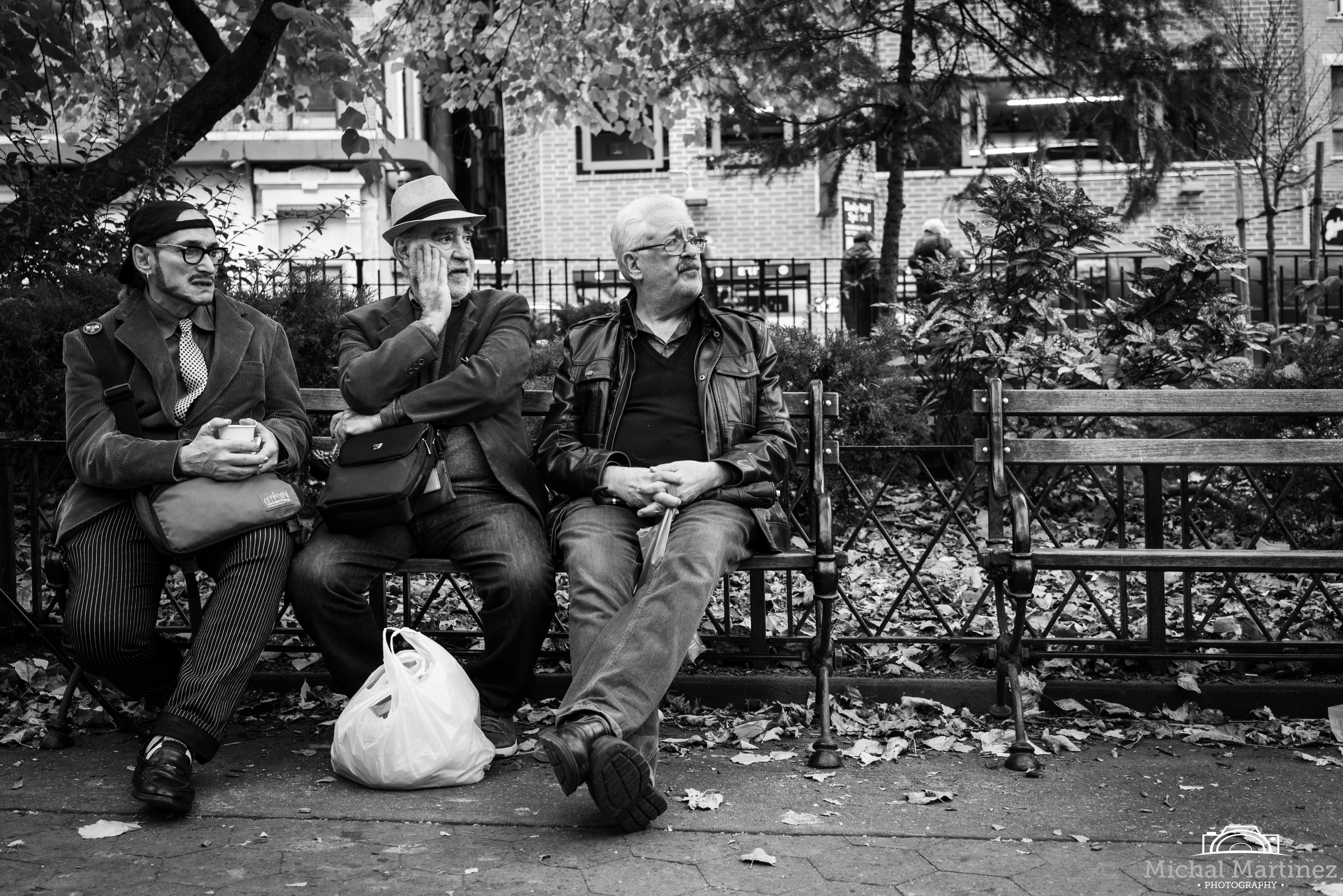 Three men sitting on a park bench looking sideways.